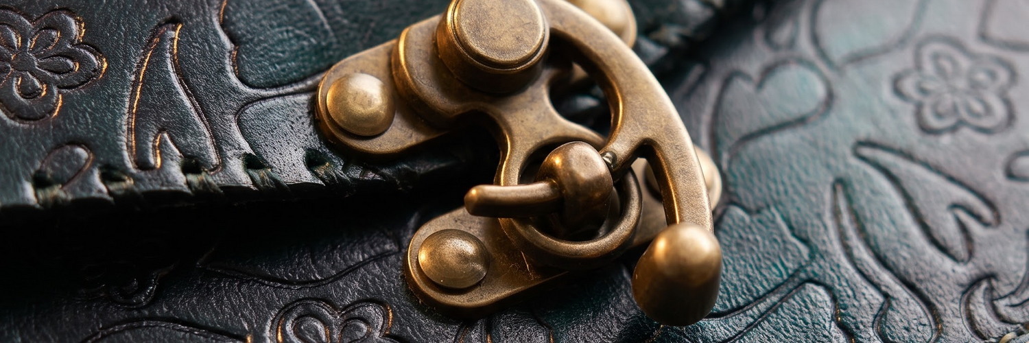 Close-up of a dark embossed leather item with an antique brass clasp and the text 'ANTIQUE BRASS HARDWARE' in the lower right corner.